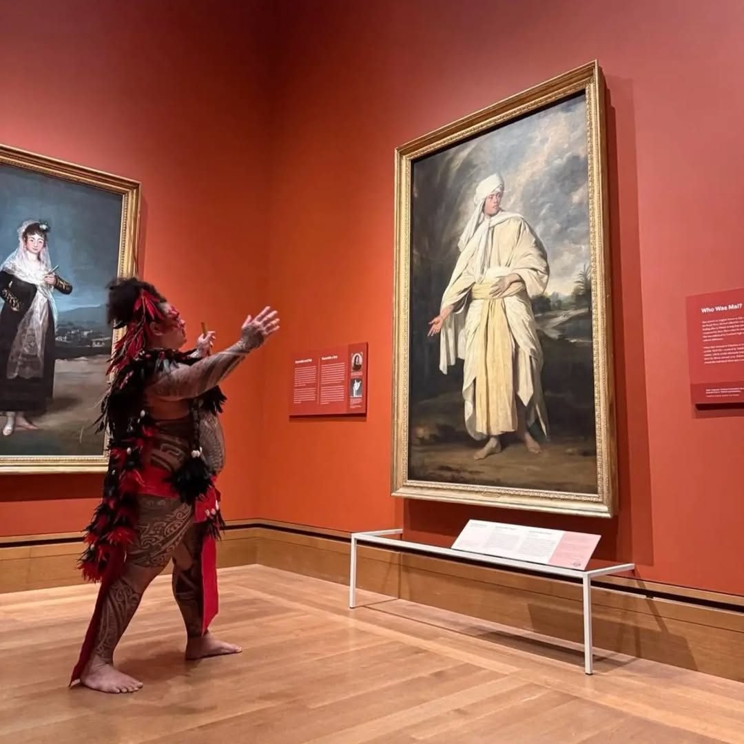 Patu en tenue traditionnelle face au portrait d'Omai, dans une salle rouge du Getty Museum
